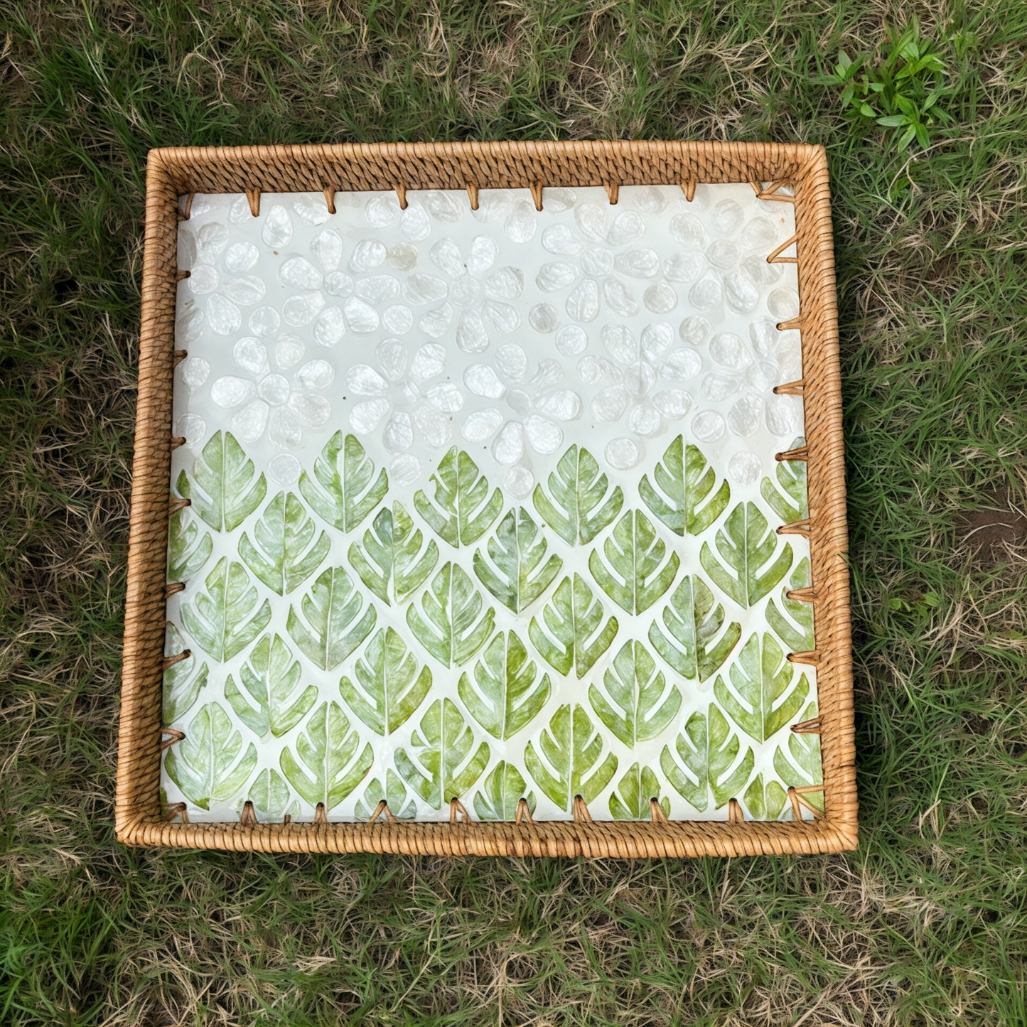 Top view of square rattan tray with green leaf mother-of-pearl mosaic placed on grass
