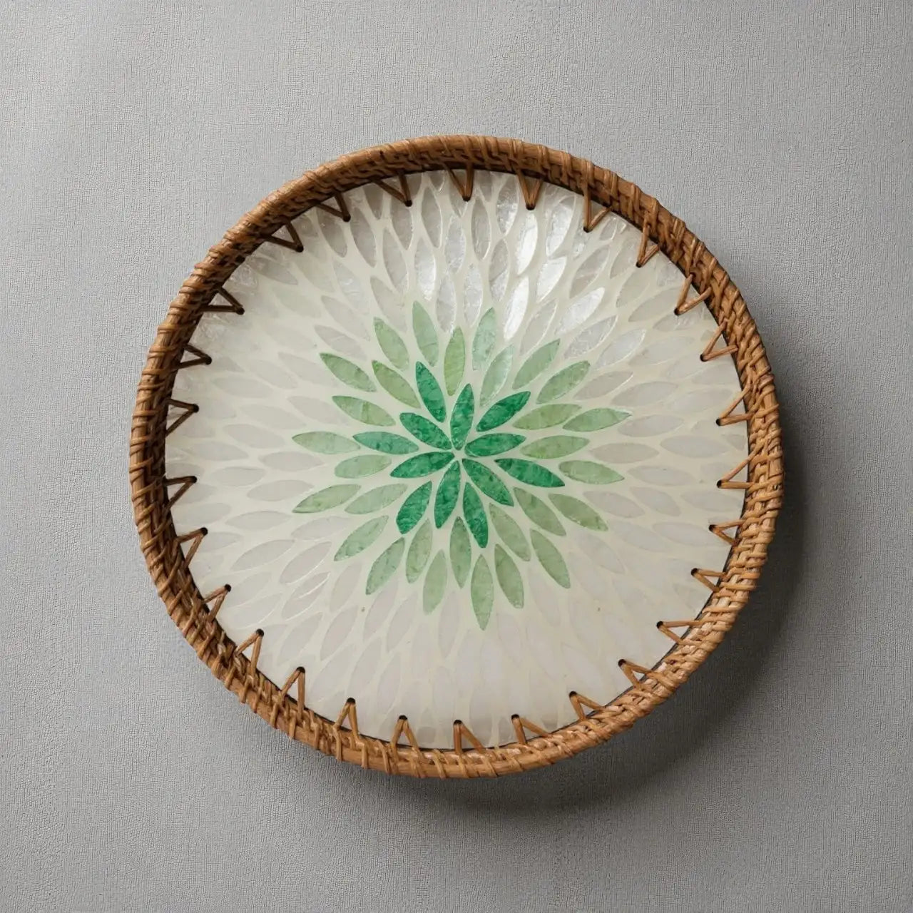 Green lotus mother-of-pearl mosaic tray with rattan rim on neutral fabric background