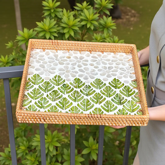 Square green leaf mosaic tray resting on a balcony railing with greenery behind