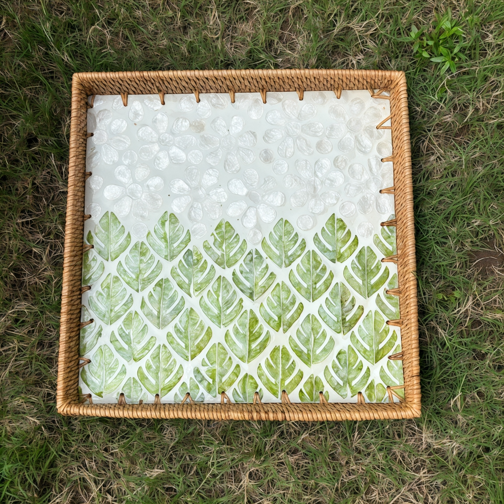 Top view of square rattan tray with green leaf mother-of-pearl mosaic placed on grass