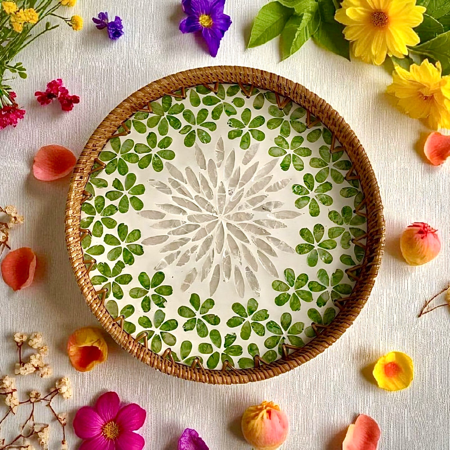 Round mother-of-pearl tray with green floral mosaic and rattan rim, styled with flowers – decorative coffee-table tray.