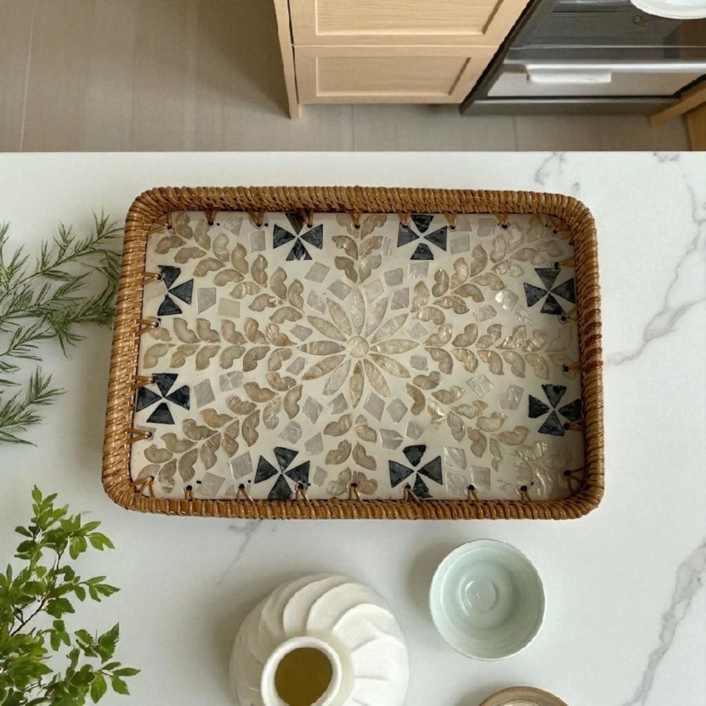 Overhead view of rectangular mother-of-pearl tray on kitchen counter with mugs and greenery.