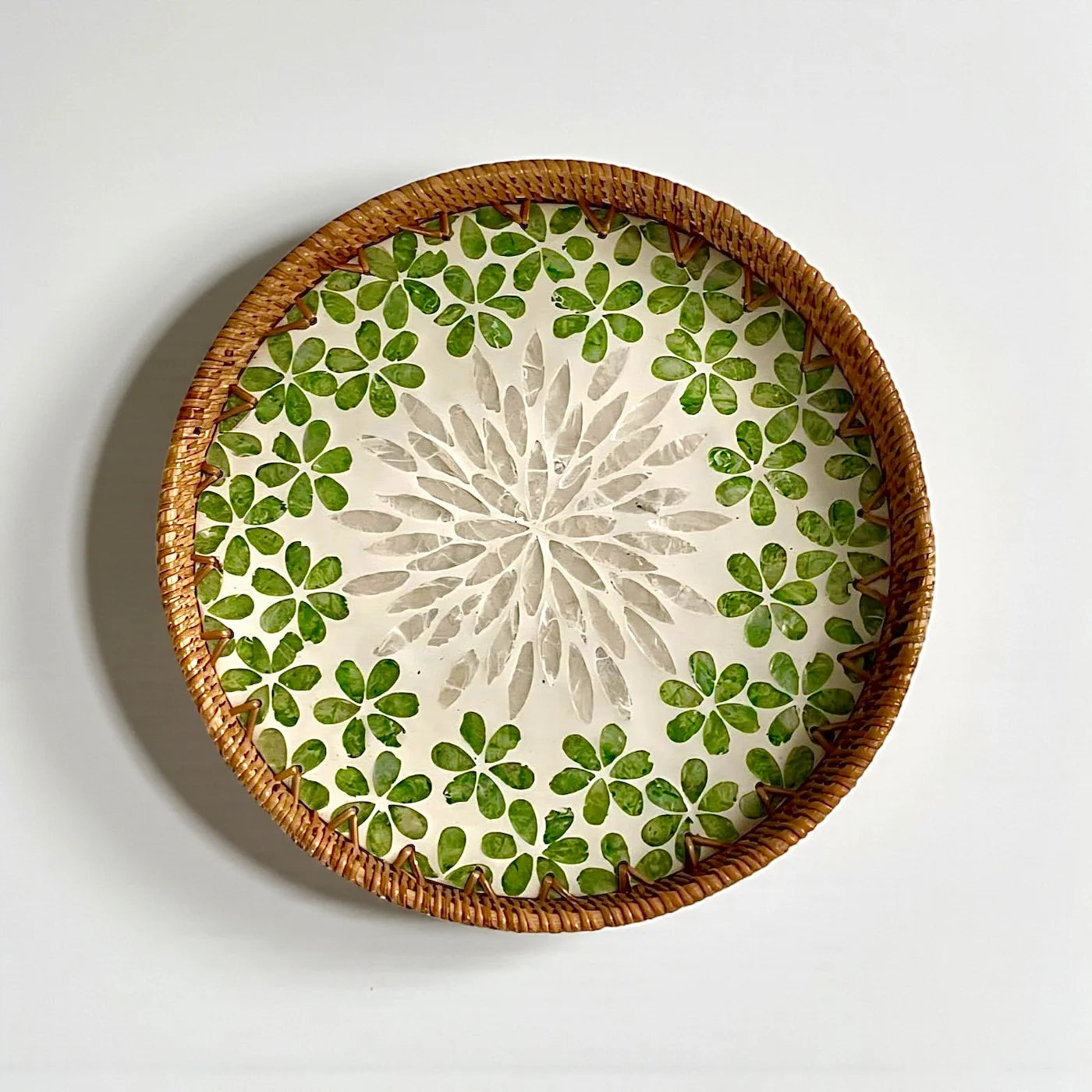 Round mother-of-pearl tray with green floral mosaic and rattan rim on a neutral background