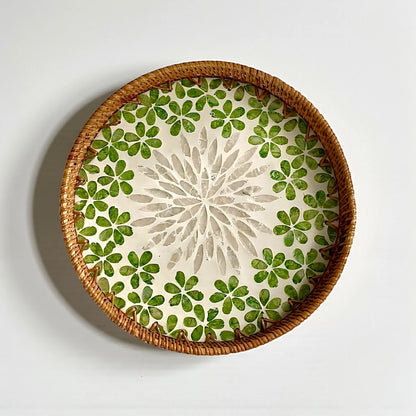 Round mother-of-pearl tray with green floral mosaic and rattan rim on a neutral background