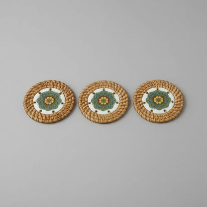 Three Meadow Mandala ceramic coasters wrapped in handwoven rattan, arranged in a row on grey background.