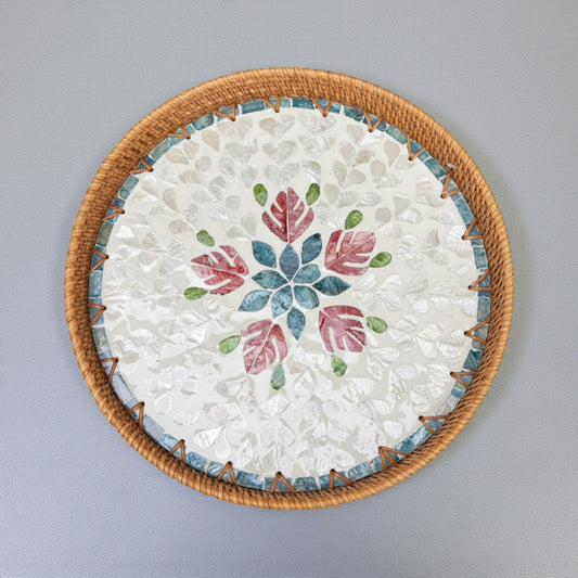 Round mother-of-pearl decorative tray with rattan rim and floral mosaic on a grey background