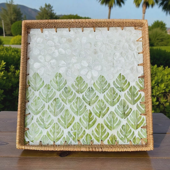 Video of square rattan tray with green leaf mosaic displayed outdoors with palm trees in the background
