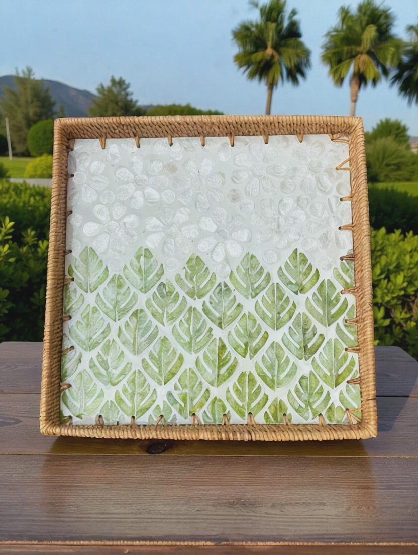 Video of square rattan tray with green leaf mosaic displayed outdoors with palm trees in the background